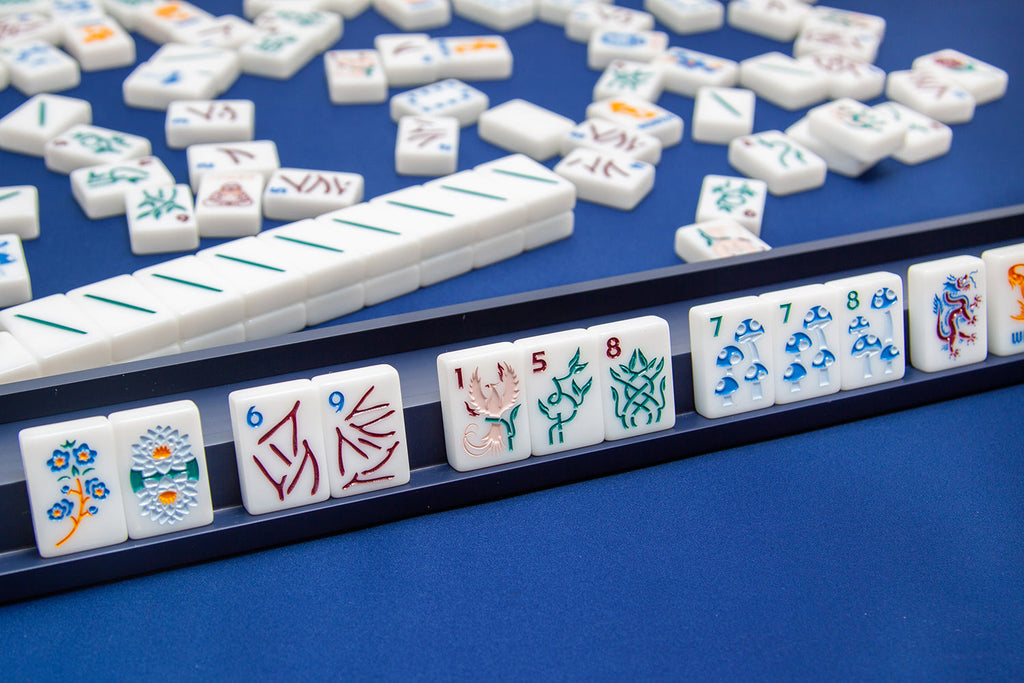  The Mahjong Line releases a new American mahjong tile set called the Joshua Tree. The mah jongg tiles are white tile on a displayed on top of the midnight blue racks and blue mah jongg playing mat.
